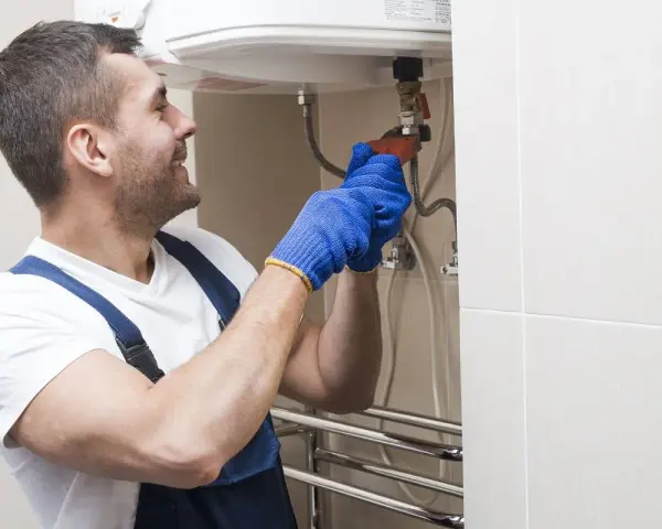 Instalator w niebieskich rękawiczkach dokręca zawór, pokazując, jak spuścić wodę z bojlera.